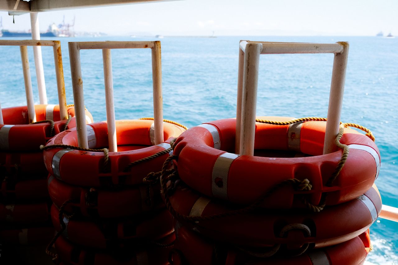 Stacks of red life buoys secured on a ship deck with a serene ocean view.
