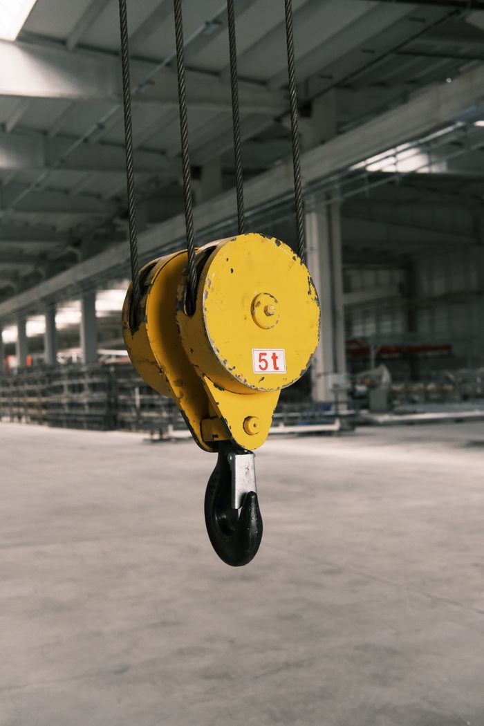 Closeup of a 5-ton yellow crane hook in an industrial warehouse setting.