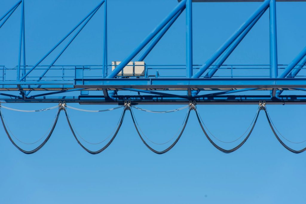 Close-up of a blue industrial crane against a clear blue sky, showcasing structure cables.