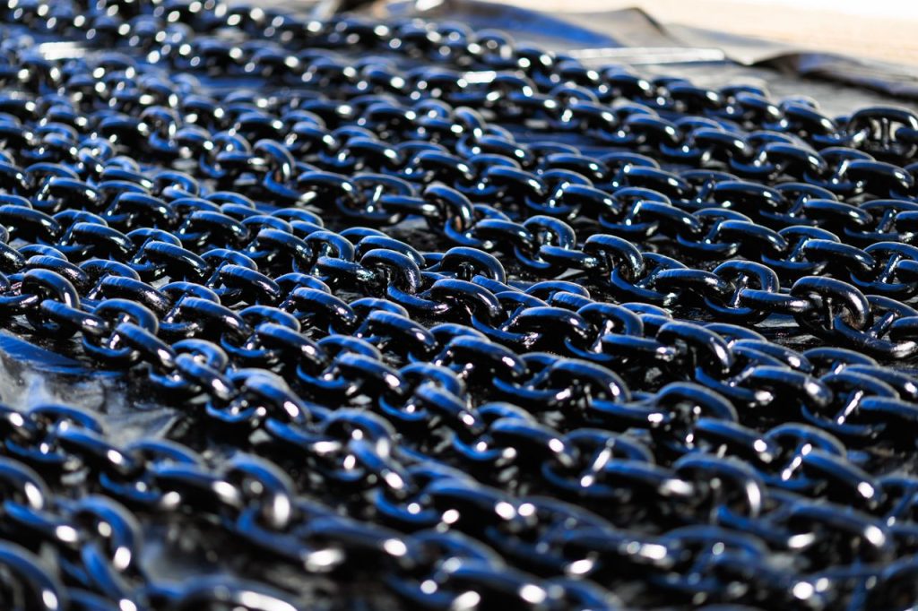 Detailed view of shiny industrial metal chains arranged outdoors, showcasing texture and metallic quality.