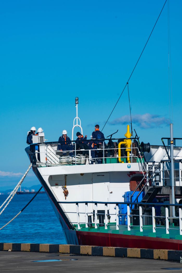 Sailors in uniform managing a commercial ship docked at a harbor under clear skies.