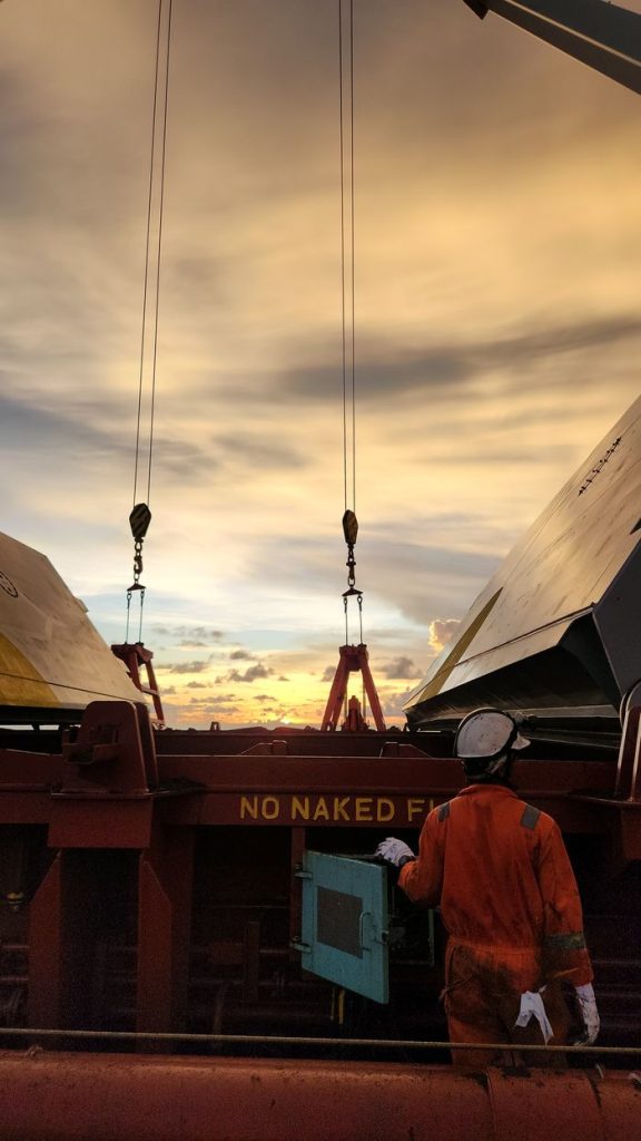 A worker in safety gear on a cargo ship at sunset, emphasizing maritime safety.